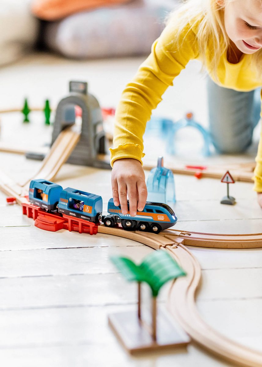 Kid playing with Brio train on floor.