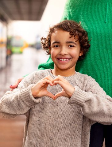 Kid making a heart with her fingers, sunlight, summer, evening, city.